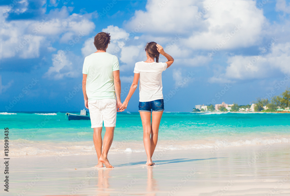 back view of happy young couple walking by the beach back view of happy young couple walking by the beach