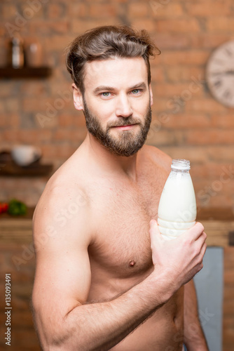 Portrait of a naked muscular man holding a bottle with milk on the kitchen