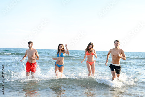 four happy friends young people man and woman having fun at ocean beach jumping together in the sea