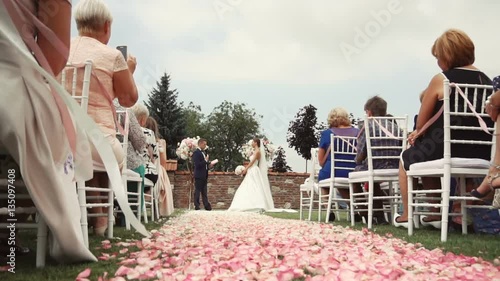 Wedding ceremony location with bride and groom, pink petals path beetwen white guests chairs
