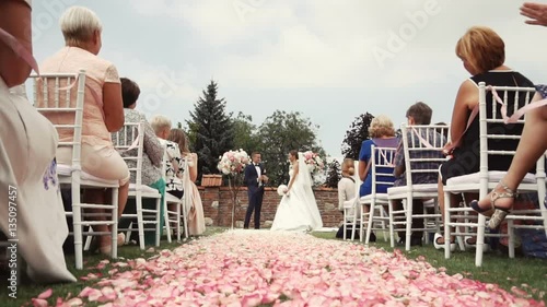 Wedding ceremony location with bride and groom, pink petals path beetwen white guests chairs photo