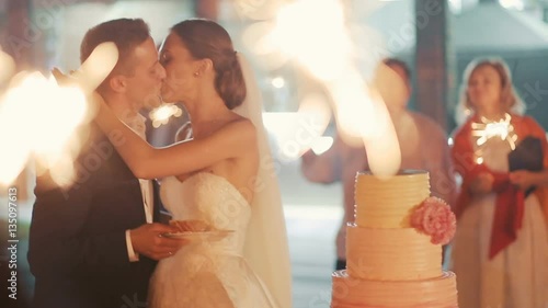 Beautiful young wedding couple eating cake, guests with sparklers