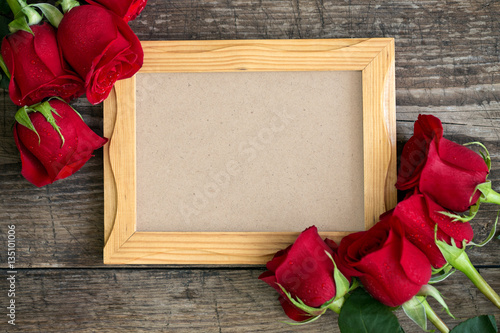 photo frame and red roses on wooden background.