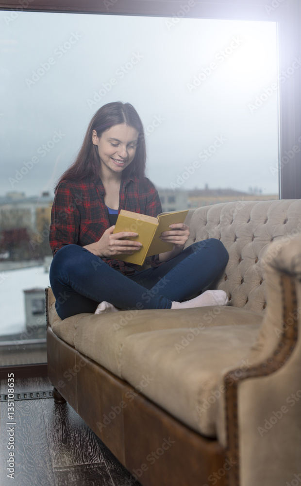 Beautiful girl in shirt sitting on the couch and reading a book. Beautiful girl in shirt sitting on the couch and reading a book.