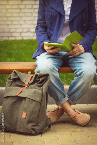 Student sitting on the bench with tablet and backpack