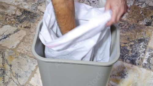 A man inserts a fresh, empty trash bag into a trashcan as part of his weekly chores.