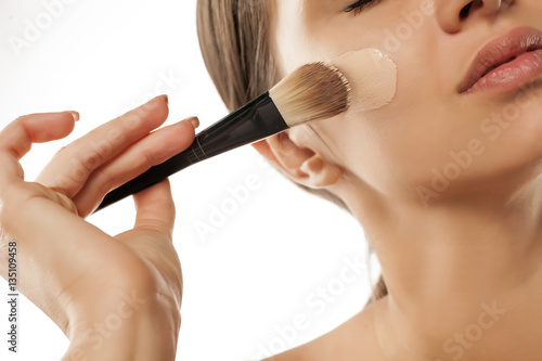 A young woman applied liquid foundation on her face with a brush photo