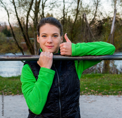 Young athlete giving thumbs up while doing pullups. photo
