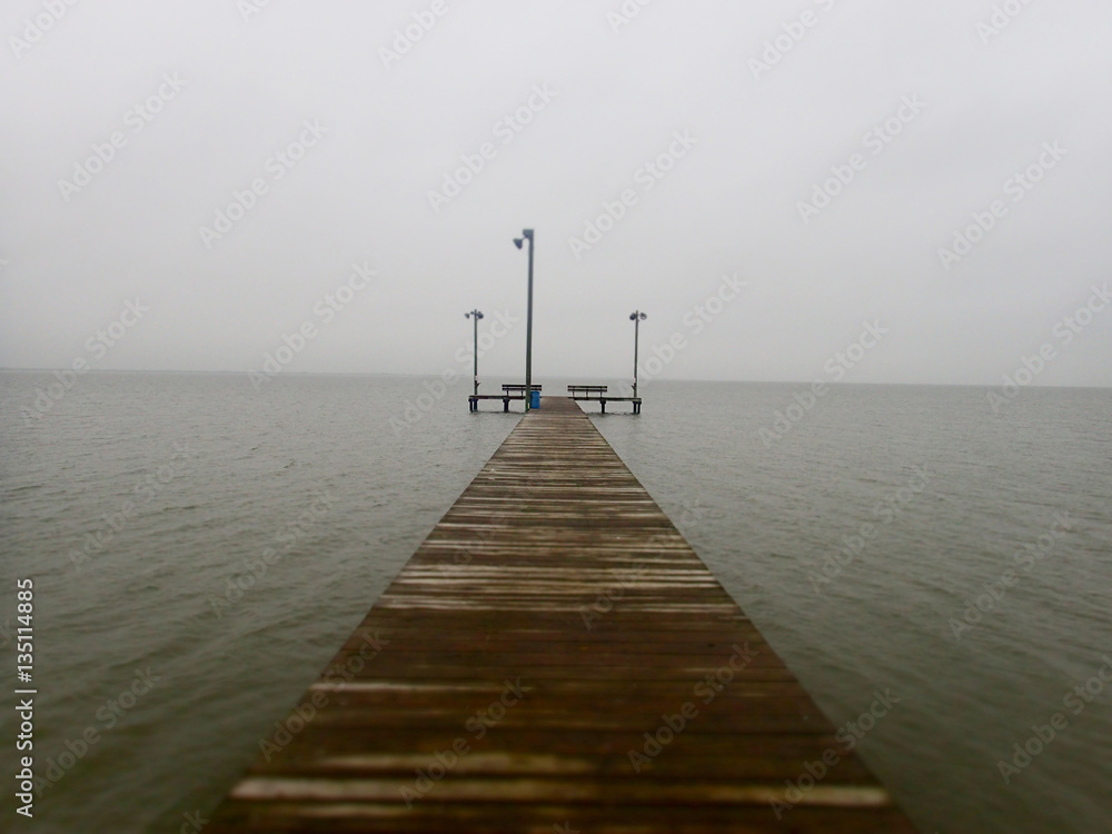 A wooden pier stretches into the ocean fog at the gulf of Mexico in Texas.