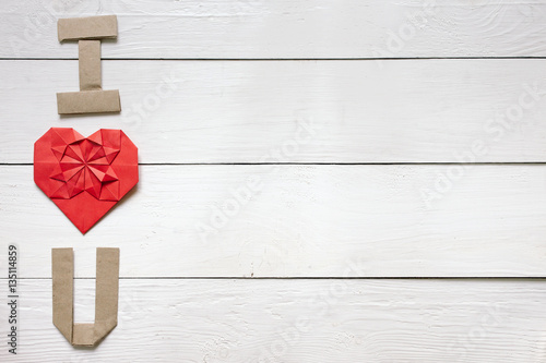 Red origami heart, craft paper folded letters I Love You (I, U) inscription on white painted rustic rural barn wood background.