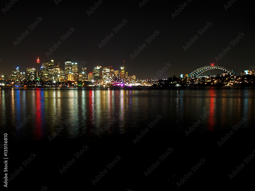 The lights of Sydney reflect in the harbor at night.