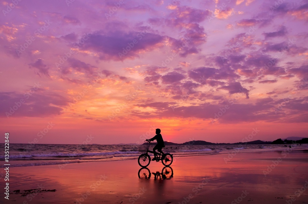 Fototapeta premium Silhouette of boy riding a bicycle on the beach with drametic sky