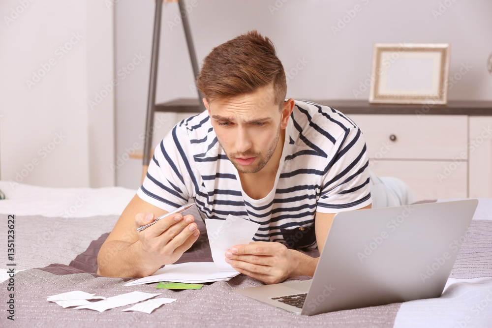 Confused young man calculating taxes at home
