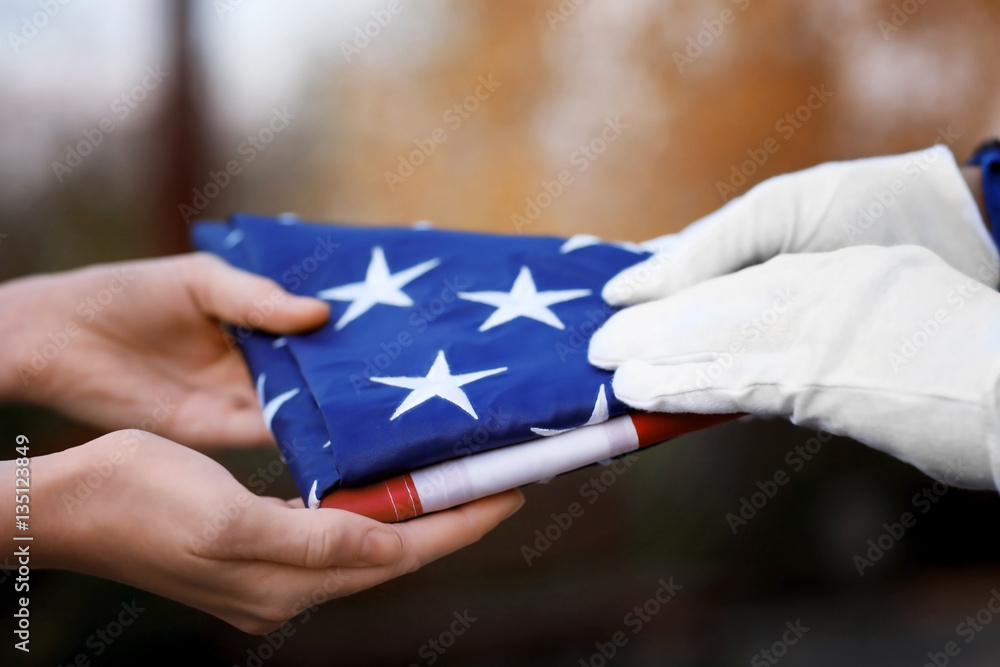 Fototapeta premium Hands holding folded American flag on blurred background