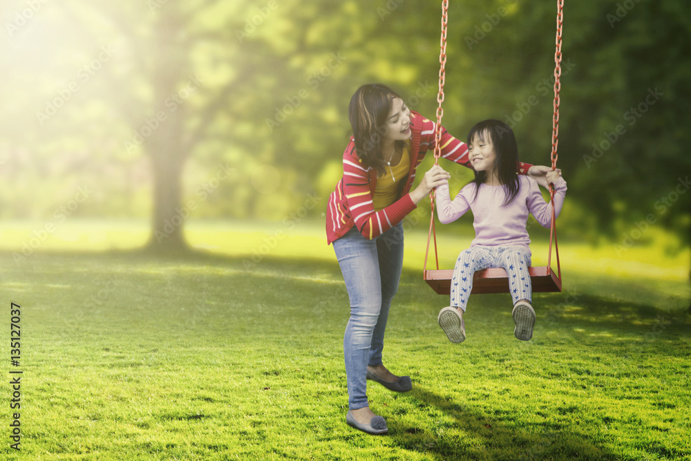 Cute child and young mother playing swing