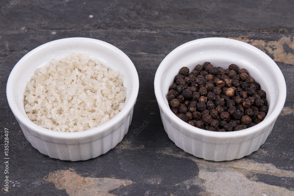 Course gray salt and peppercorns in smal ramekins on gray slate Course gray salt and peppercorns in smal ramekins on gray slate