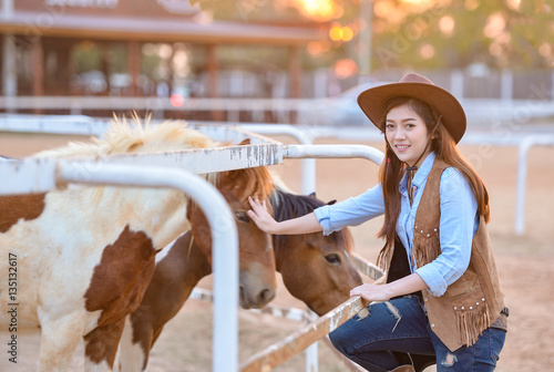 Beautiful womam sensuality elegance woman cowgirl on during sunset, riding a horse. Clothed blue jeans, brown leather jacket and hat. Has slim sport body. People and animals. Equestrian. vintage style