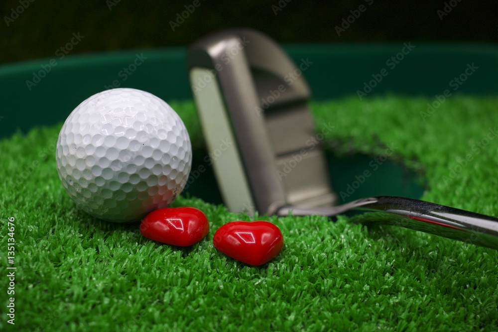 Naklejka premium Golf ball and putter with heart are on green grass