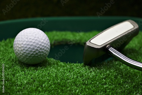 golf ball and putter are next to the hole.