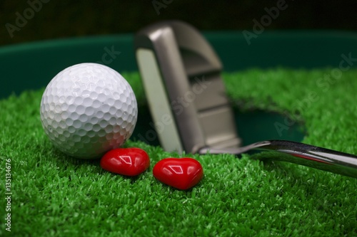 Golf ball and putter with heart are on green grass