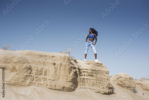 Beautiful Black African American fitness athlete in the desert wearing a bright fitness outfit  standing strong on the edge of a sandy cliff 