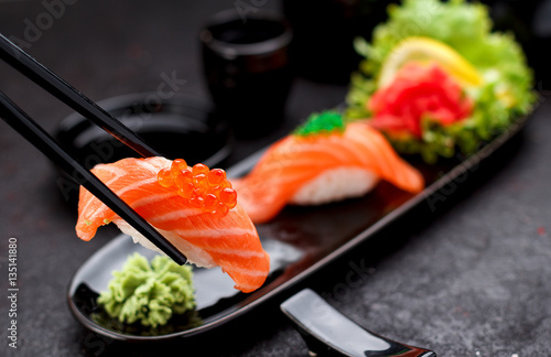Japanese cuisine. Salmon sushi nigiri on a black plate with chopsticks.