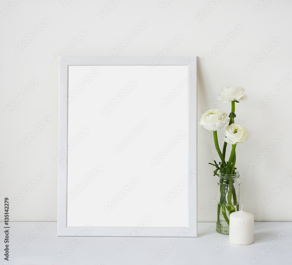 Empty white frame with place for text on the white wall and table, bouquet of flowers ranunculus and candle. Scandinavian style room interior. Template mock up for paintings or photographs