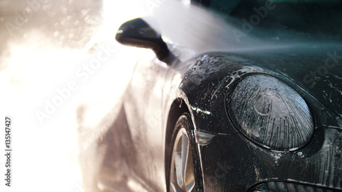 Canvastavla Worker in auto service is washing a luxury car by water hoses, backlight