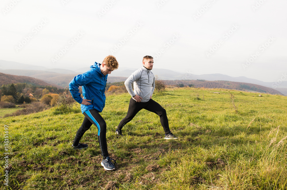 Two young hipster runners in sunny autumn nature stretching legs