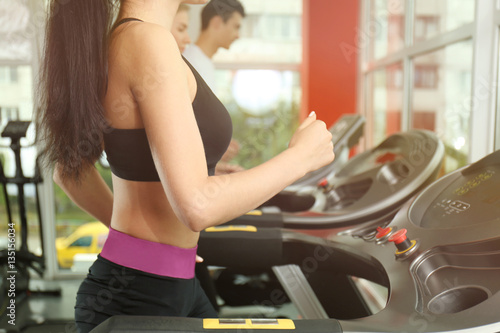 Young sporty woman running on treadmill in gym, close up view