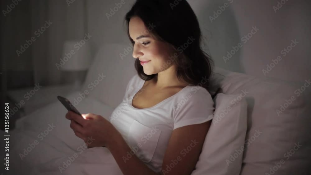 happy young woman with smartphone in bed at night happy young woman with smartphone in bed at night