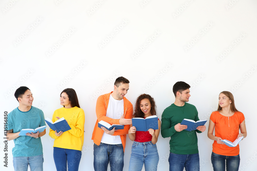 Group of people reading books while standing near light wall Group of people reading books while standing near light wall