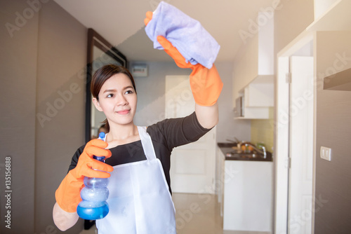 Asian young maid cleaning the mirror with spray at home, Cleaning service concept
