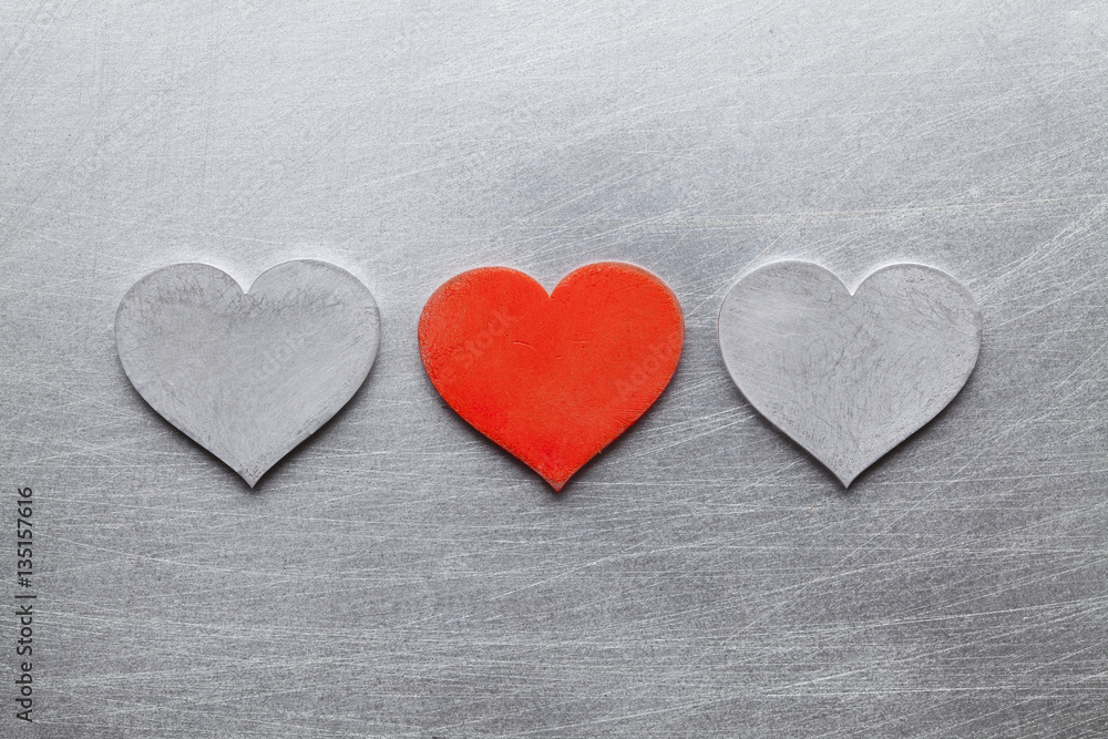 Two silver and one red metal hearts on scratched surface