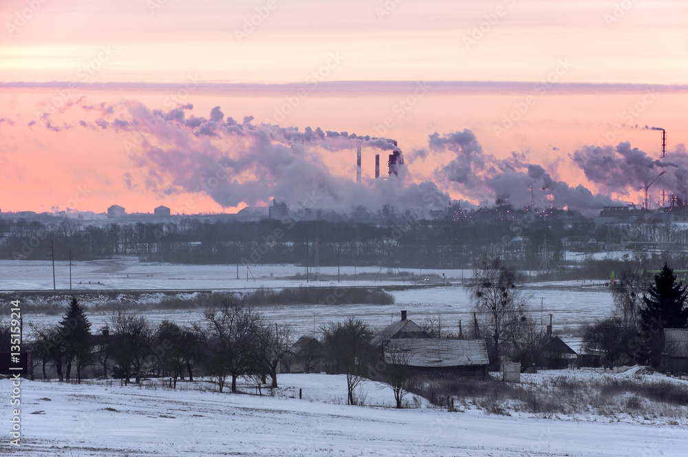 Fototapeta premium Working Nitrogen Plant in smoke on the background of dawn in winter. Abandoned village in the foreground. Grodno, Belarus.