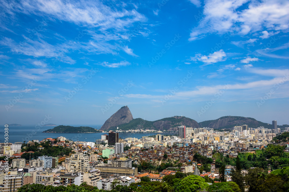 Urban view of Rio de Janeiro city with Sugarloaf Mountain, residential houses and a nearby slum favela adjacent to the hillside of Santa Teresa district