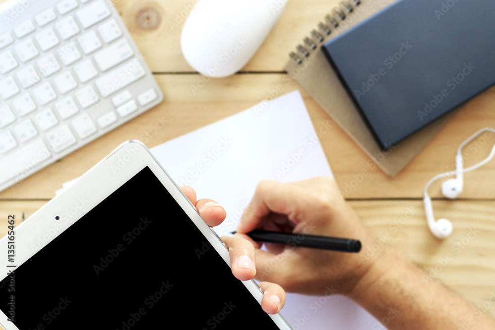 female hands holding a computer tablet and writing on paper with table in the office. soft-focus in the background. over light female hands holding a computer tablet and writing on paper with table in the office. soft-focus in the background. over light