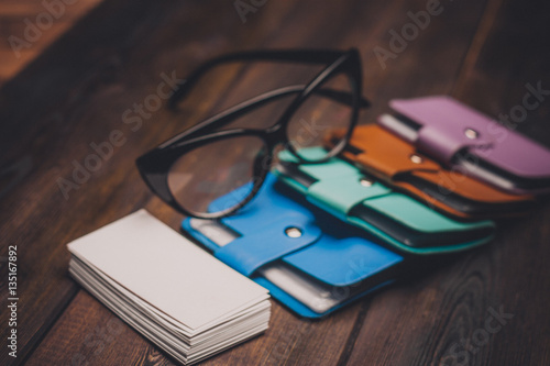 notebooks of different colors, paper, wooden background, glasses