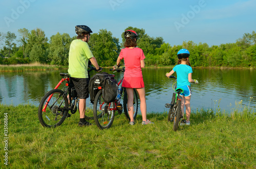 Family on bikes outdoors, active parents and kid cycling and relaxing near beautiful river, fitness concept 