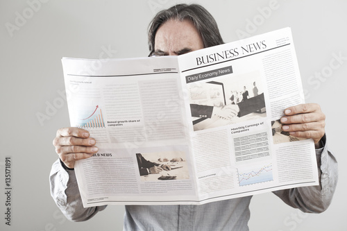 Senior man reading newspaper on gray background