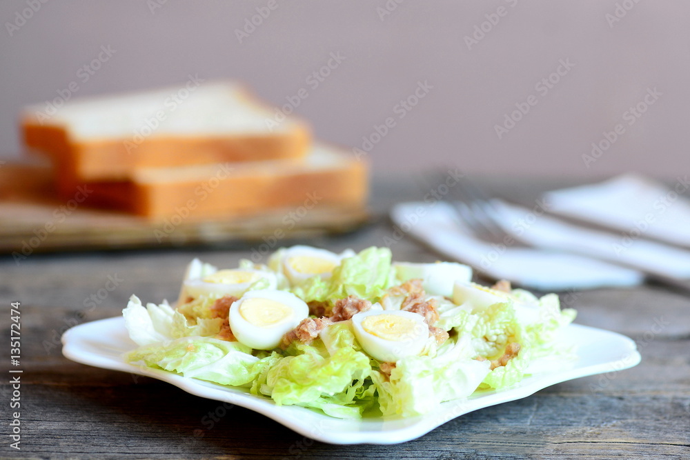 Chinese cabbage salad with canned tuna and quail eggs dressing with olive oil and lemon juice. Cabbage salad on plate, bread slices on wooden table. Simple and quick salad recipe. Closeup