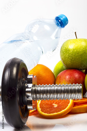 Concept of healthy active life. Heap of fruits, green and red apples, red oranges, slices of red orange, Fitness dumbbell. Bottle with pure drinking water. Healthy diet nutrition,White background.