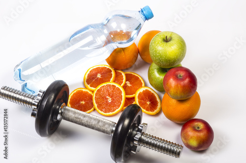 Concept of healthy active lifestyle. Heap of green and red apples and red oranges. Bottle of pure water . Fitness dumbbell in foreground. Sliced red orange. Healthy diet for slim body.