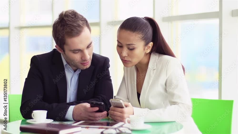 Two employees with cellular phones interacting in office Two employees with cellular phones interacting in office