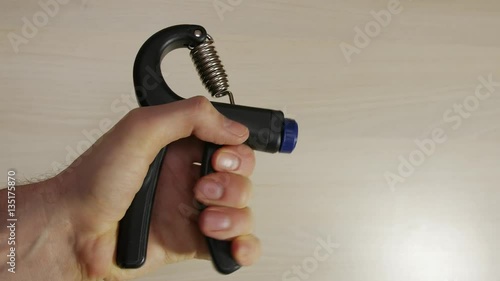 Man squeezes hand grip, strengthens muscles in hand, fingers, wrist, arm, as part of routine exercise workout, light background. photo