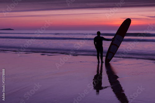 Silhouette of surfer man standing on beach at sunset holding surfboard © Tom Eversley