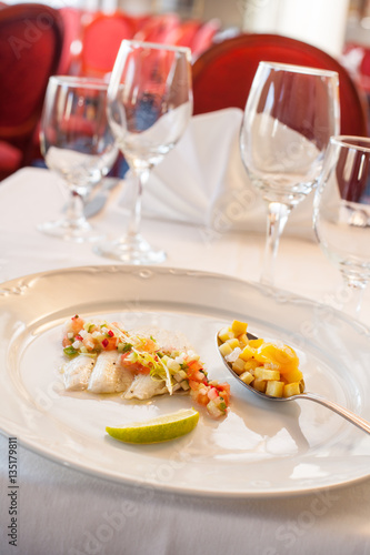 Marinated bass fillet with vegetable salad and fried potatoes with quail egg. On restaurant style background with wine glasses.