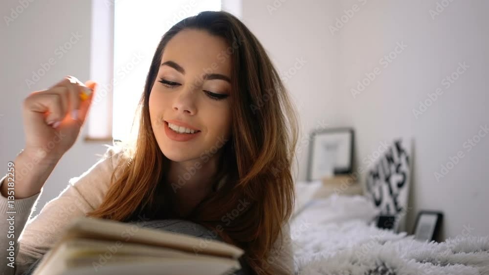 Happy young woman with pencil and notebook writing in bed at home bedroom Happy young woman with pencil and notebook writing in bed at home bedroom