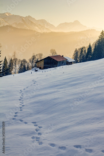 Footprints in snow towards wooden cabin in mountains of Allgau