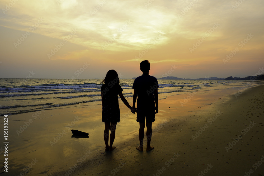 Couple holding their hands at the beach looking the sun set